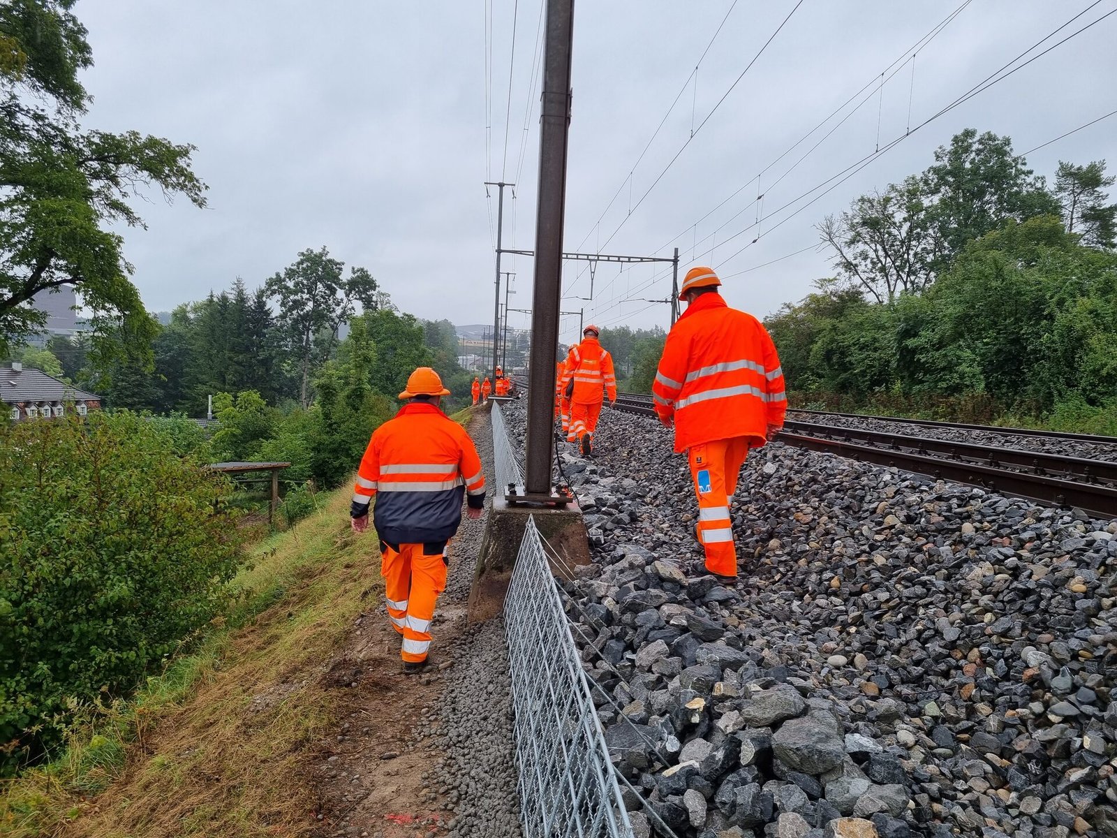 Cuadrilla de trabajo caminando junto a la vía en día lluvioso