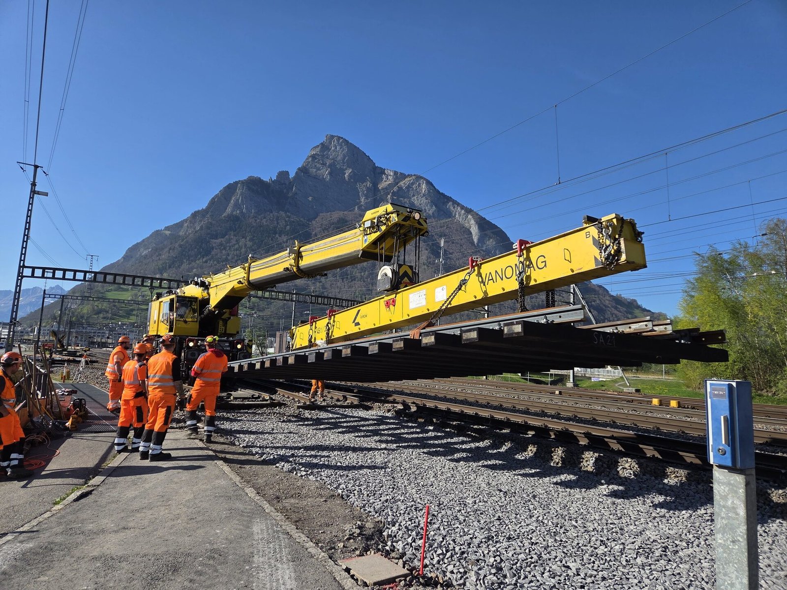 Grúa pórtico colocando rieles en la red ferroviaria suiza, con montañas al fondo
