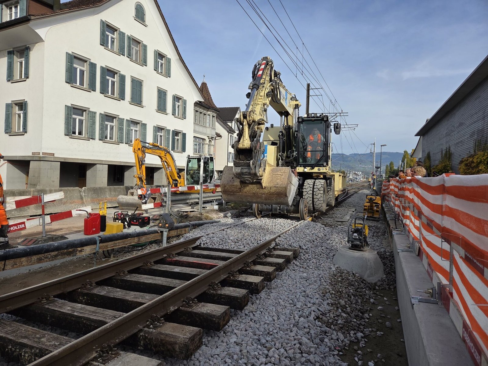 Cuchara de excavadora colocando balasto durante renovación de vía en zona urbana suiza