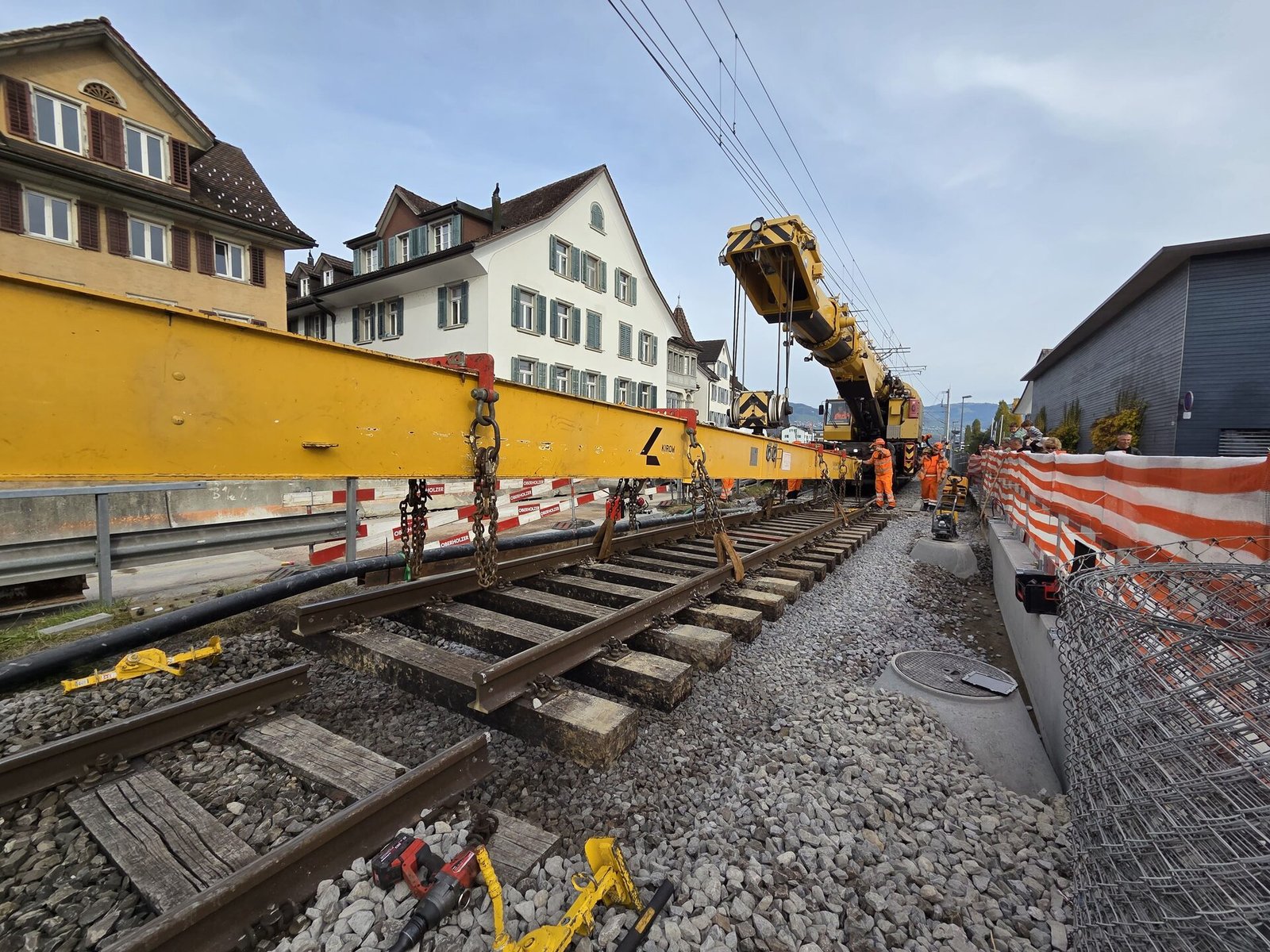 Grúa Kirow izando viga de vía durante renovación en zona urbana suiza